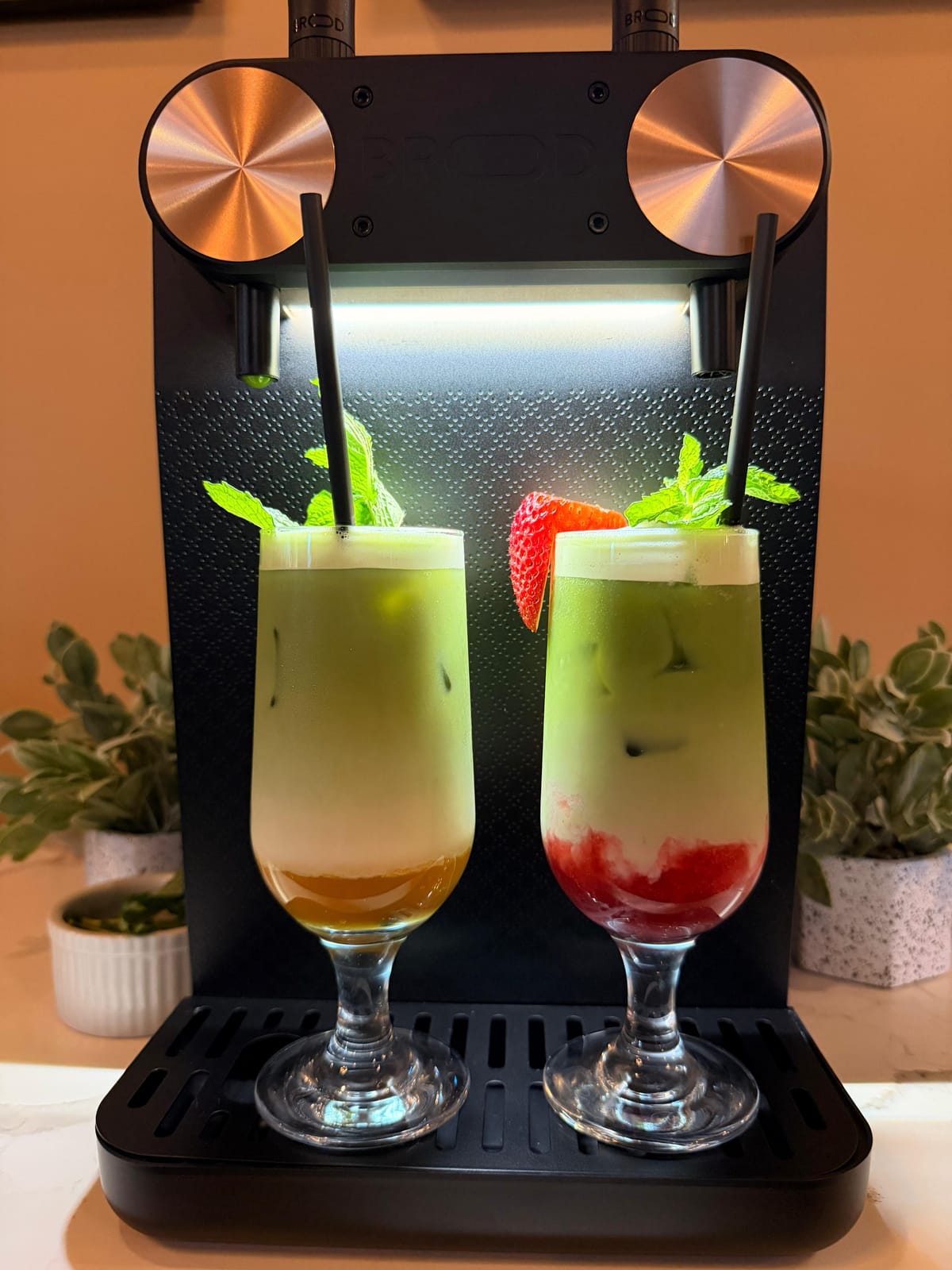 Two nitro matcha lattes, one layered with fresh strawberry, garnished with mint and a strawberry slice