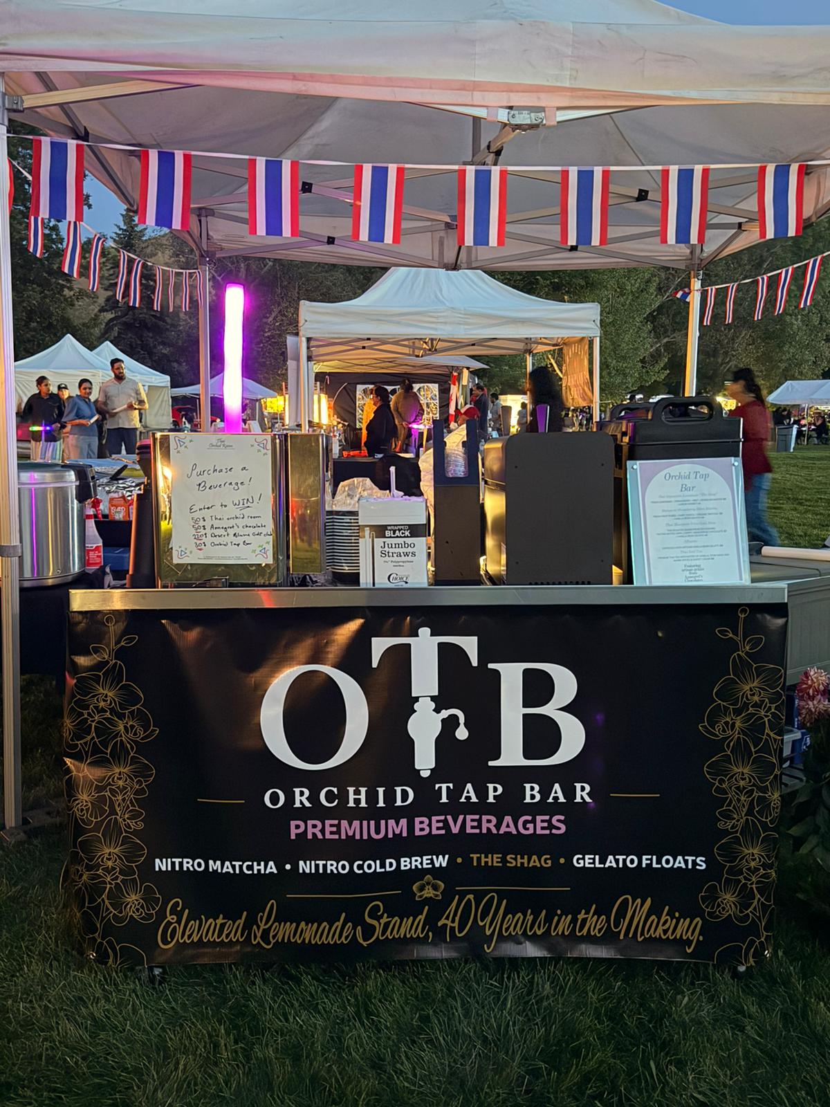 The lit OTB booth glowing at dusk with a busy festival crowd behind it