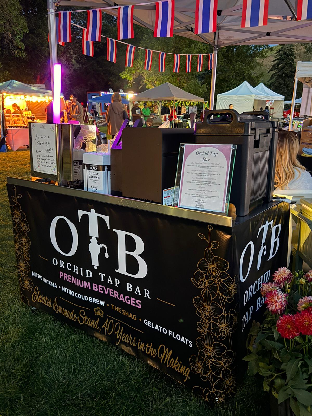The OTB booth lit up at night, framed by festival bunting