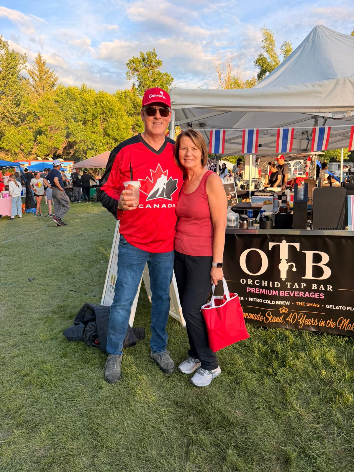 A couple in Canada colours posing with an OTB drink in front of the booth